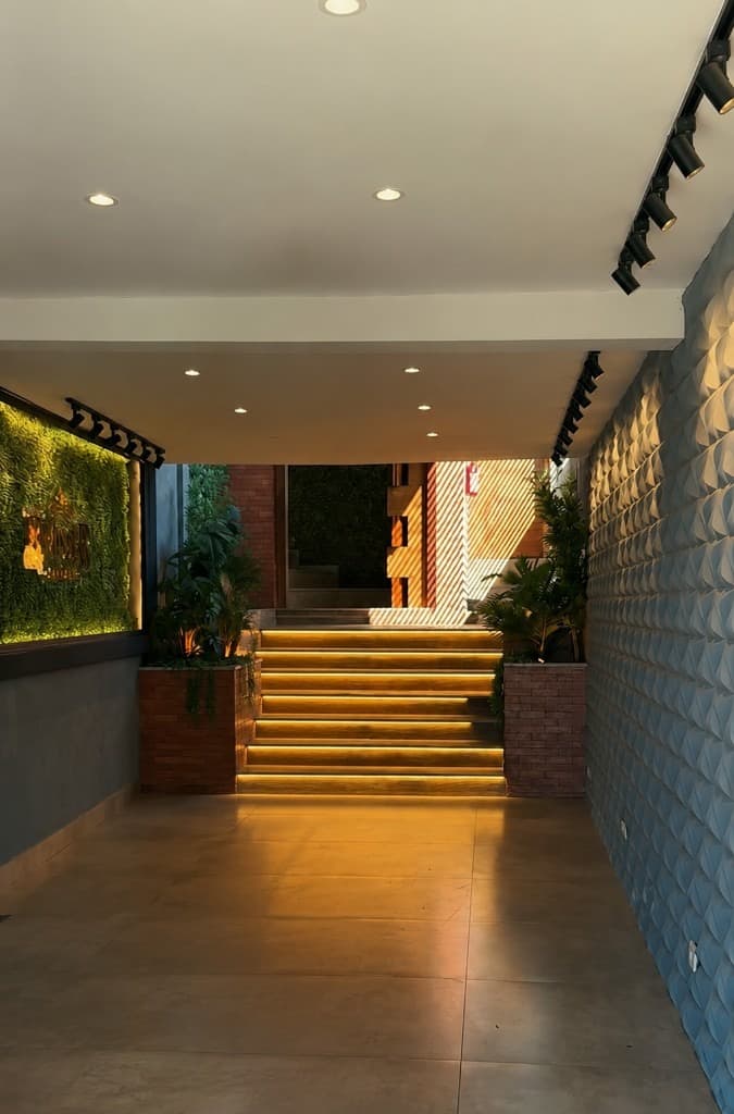 Foyer com escada iluminada, parede verde e revestimento geométrico