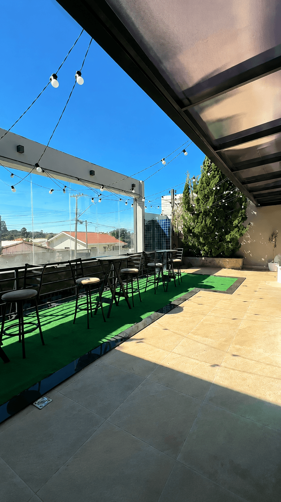 Varanda com banquetas altas, guarda-corpo de vidro e vista do bairro