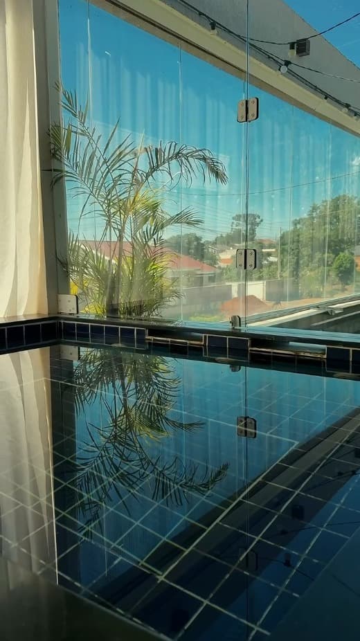 Piscina com azulejos azuis, guarda-corpo de vidro e palmeira decorativa